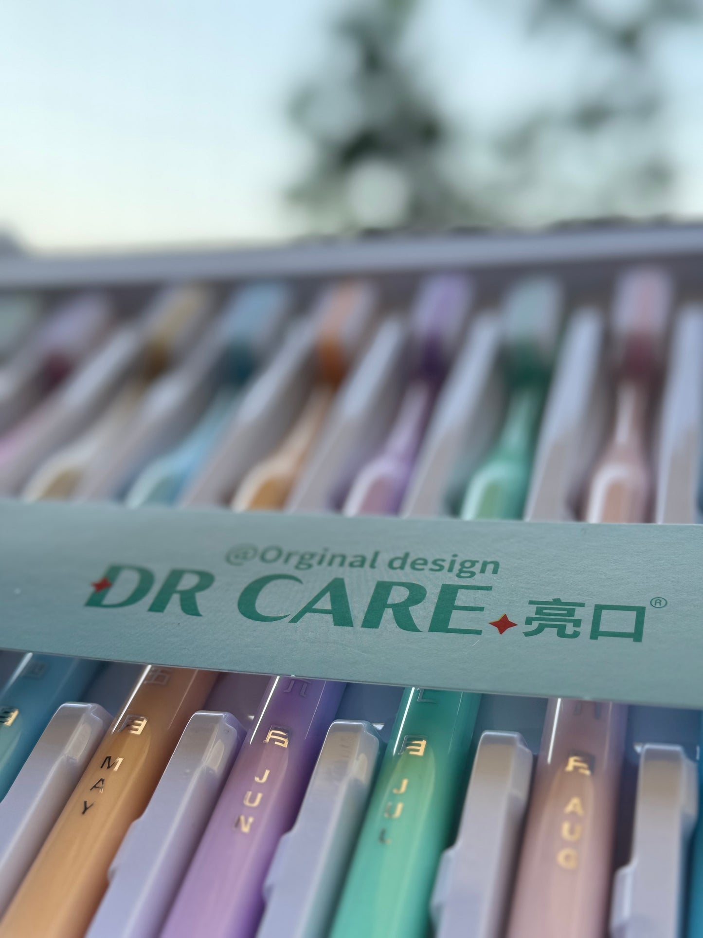 Box of DR CARE dental tools with colorful handles on a blurred natural background