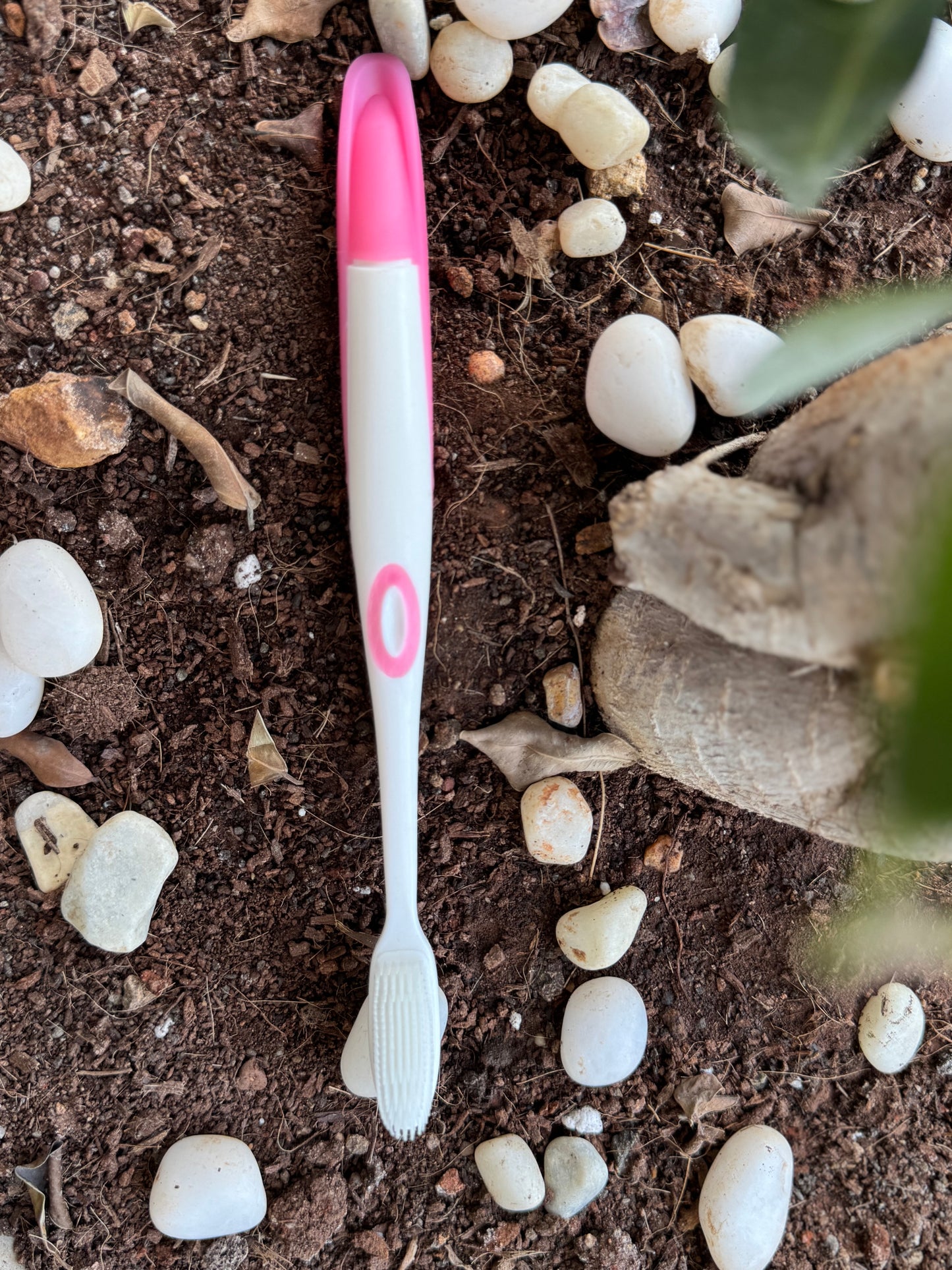 Pink and white toothbrush on a soil surface with stones and a glove.